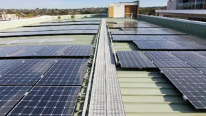 Solar panels installed on a flat, green metal roof with metal walkway weaving between.