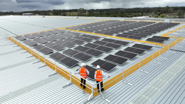 Workers stand on FRP non-slip walkway looking over the solar panel installation on a warehouse roof.