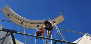 Workers installing a fall protection system on a large satellite dish.
