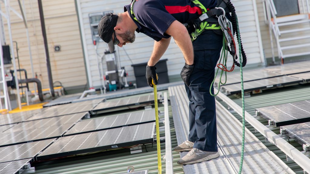 HSE technician checking an anchor point is still compliant following solar panel installation on a commercial building roof.