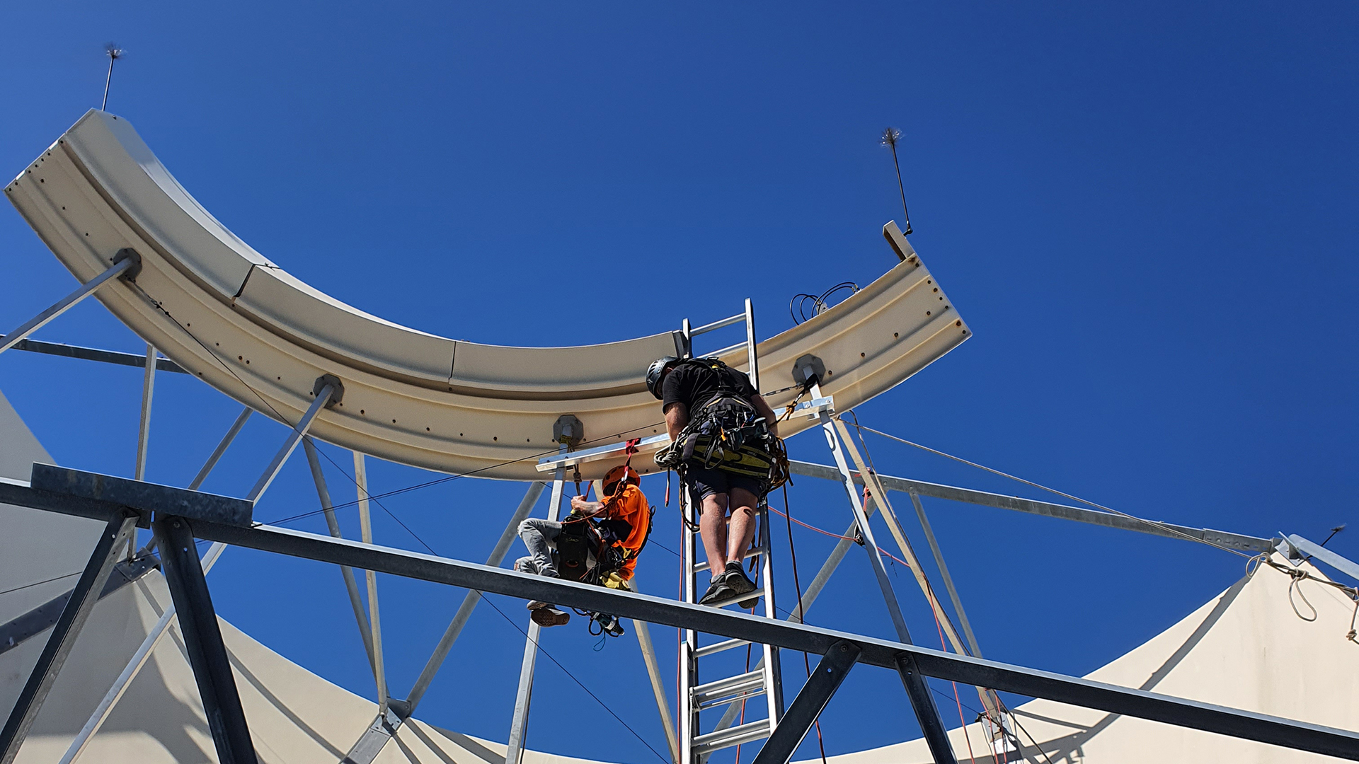 Contractors installing fall protection on a satellite receiver on top of a multi-storey building.