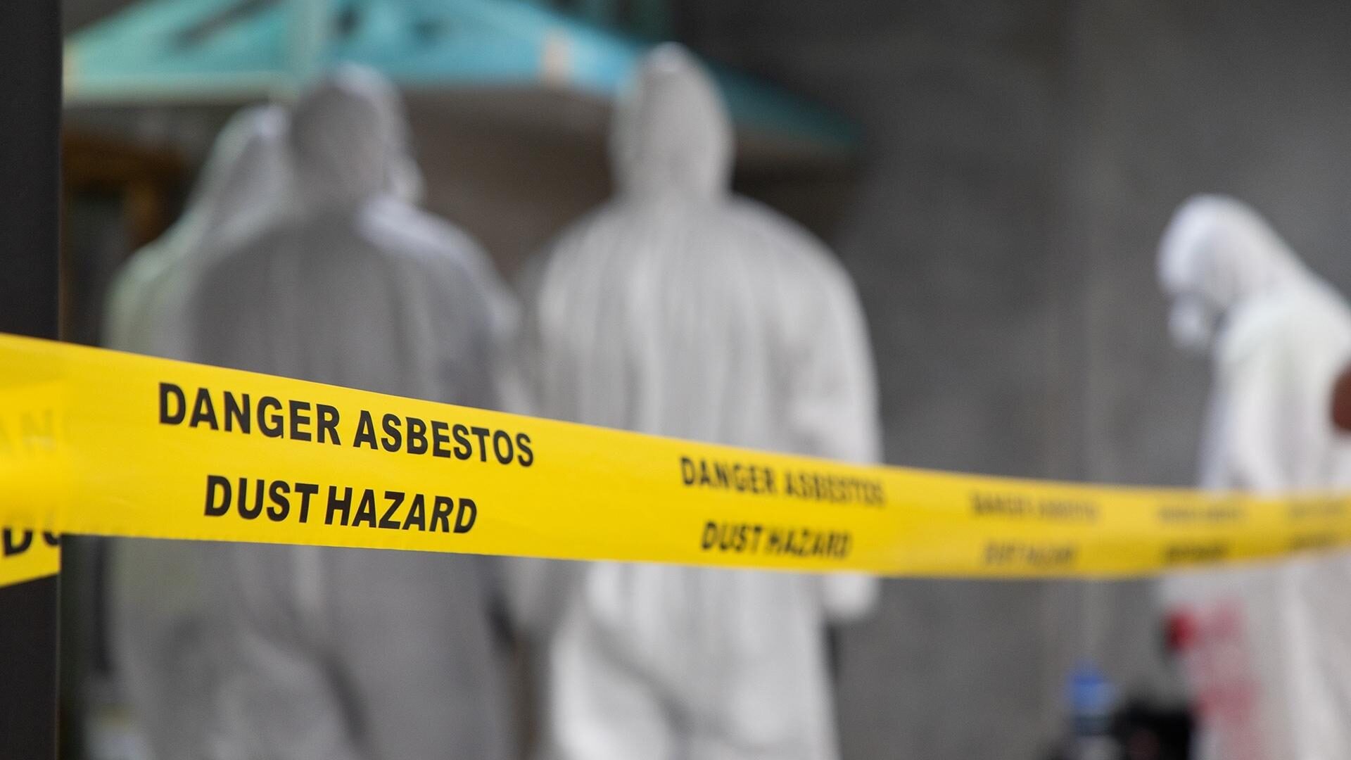 Workers in PPE behind "danger asbestos" warning tape.