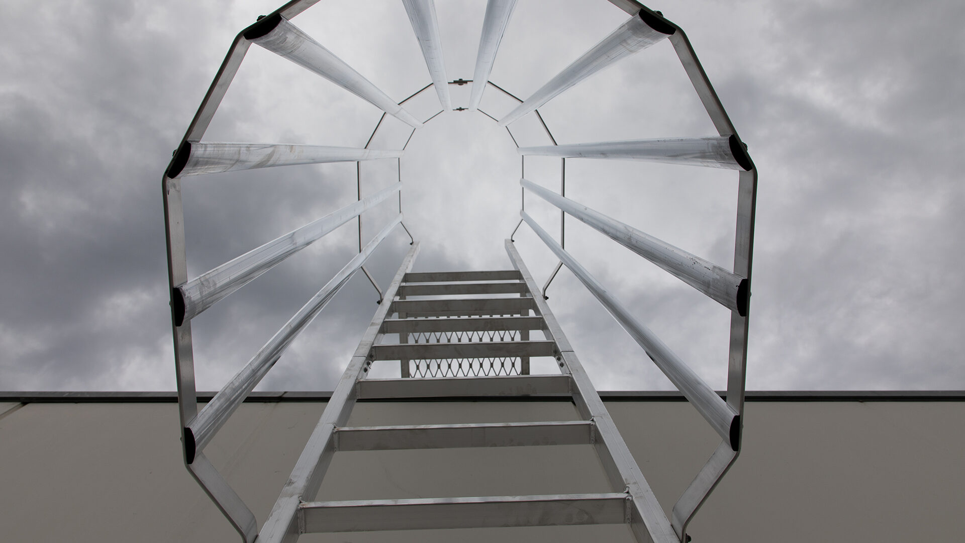 Looking up a fixed ladder, through an installed ladder cage, to the sky.