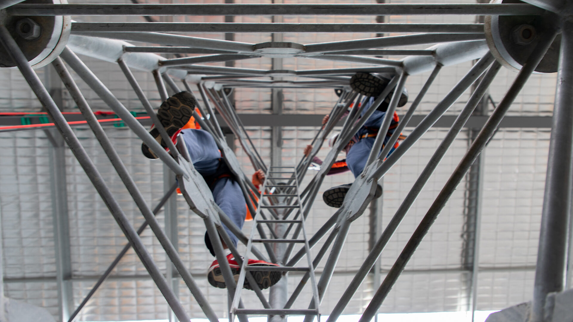 Looking up through the centre of a communications tower to workers climbing it.