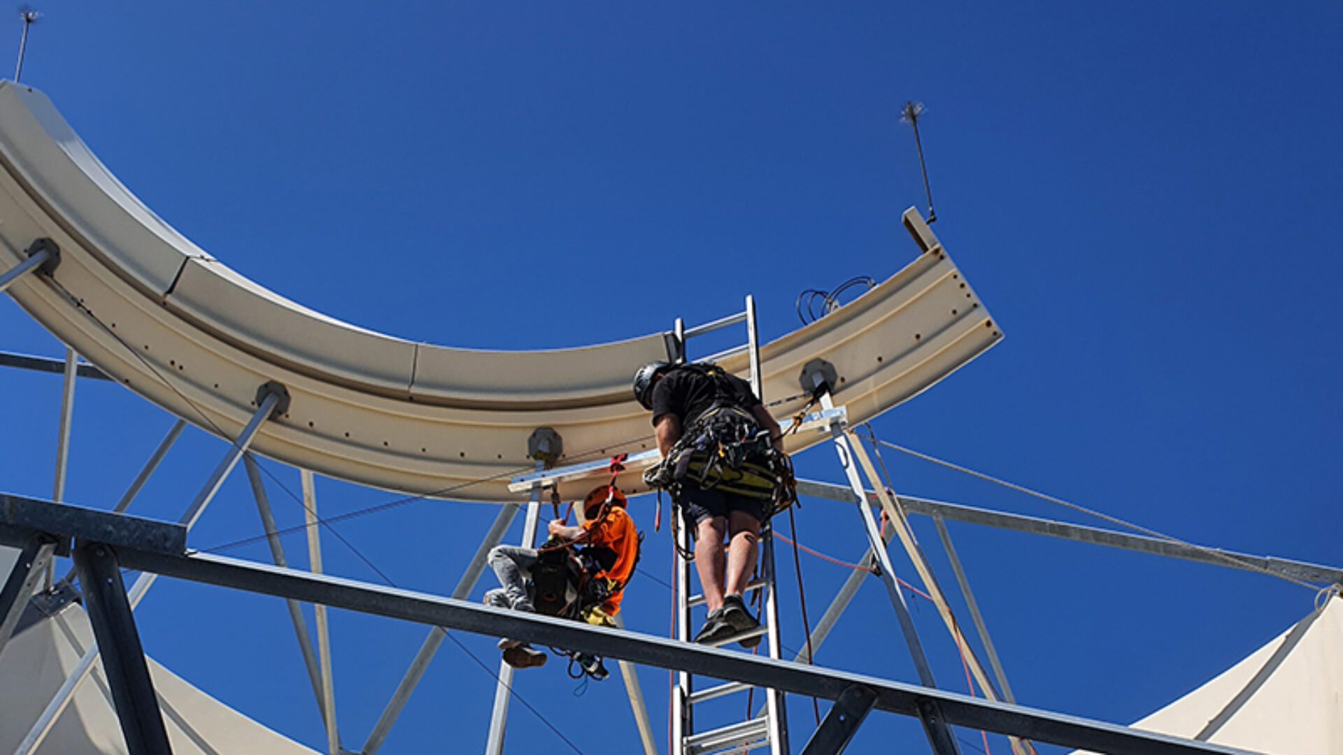Workers installing a fall protection system on a large satellite dish.