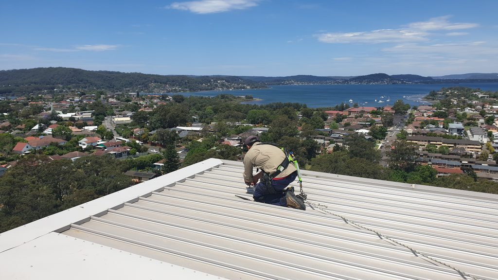 Installing a roof anchor point on the metal roof of a building.