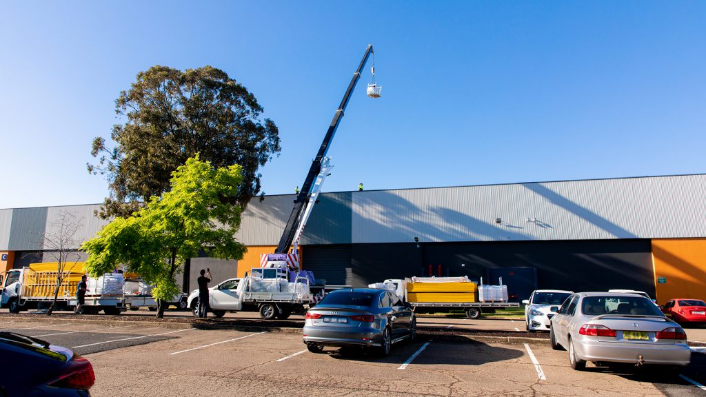 Crane lifting safety system components onto the roof of a warehouse so they can be installed.