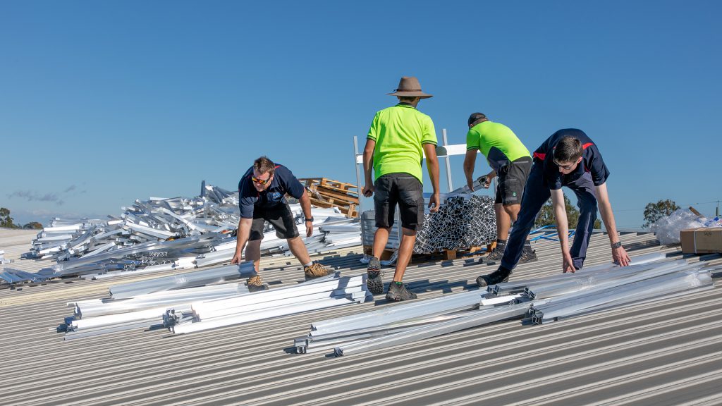 Workers preparing for the installation of a system on a warehouse roof by sorting through all the components required.