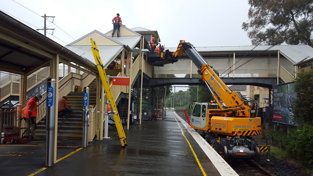 Installing a fall protection system on the roof of a railway station using a crane.