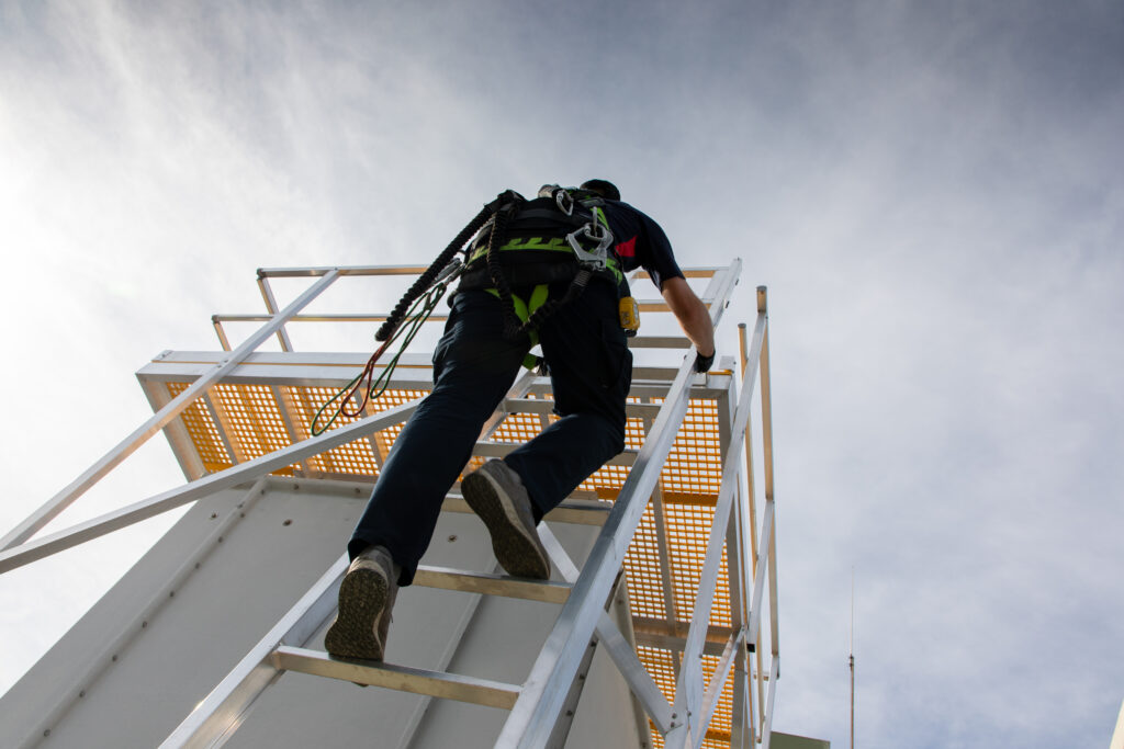 Recertification technician climbing a ladder to access the platform built around the top of a HVAC cooling tower.