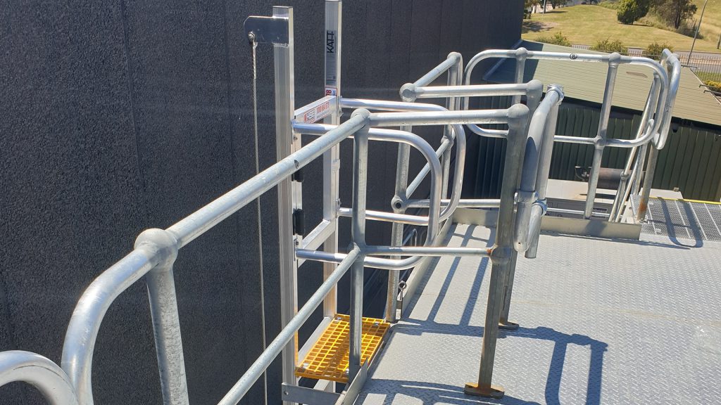 Roof access system of a fixed ladder with fall arrest line, self-closing gate and step platform.