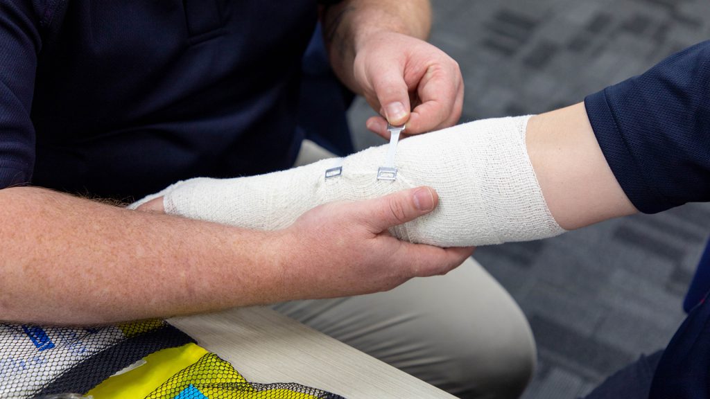 Training participant placing a bandage over a pretent wound during first aid training.